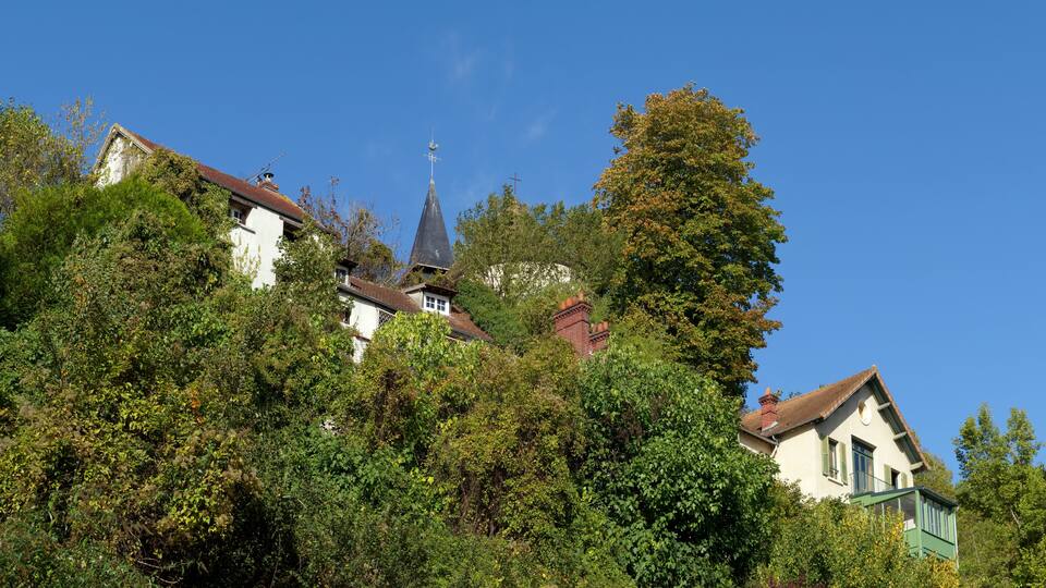 A hillside with buildings, including a church with a steeple, surrounded by dense foliage.