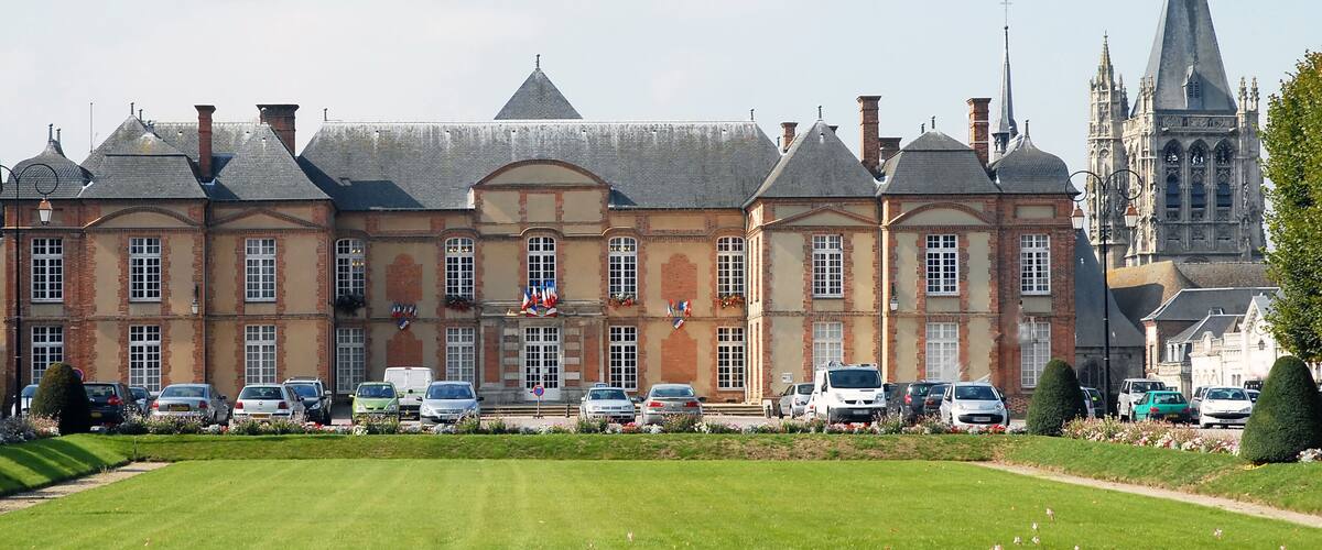 A historic building with a large lawn and parked cars in front.