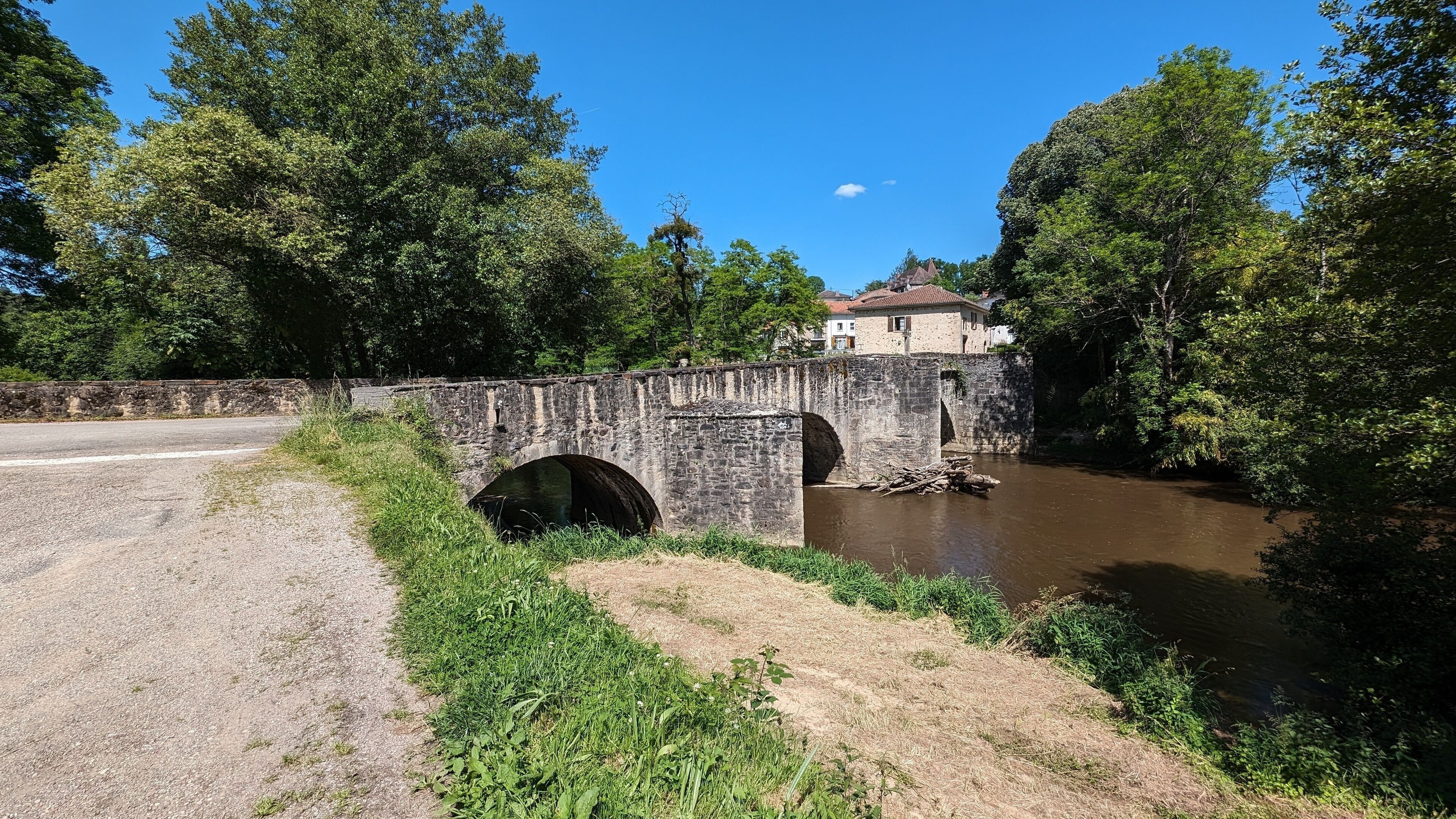 A stone bridge over a river with a house in the background.