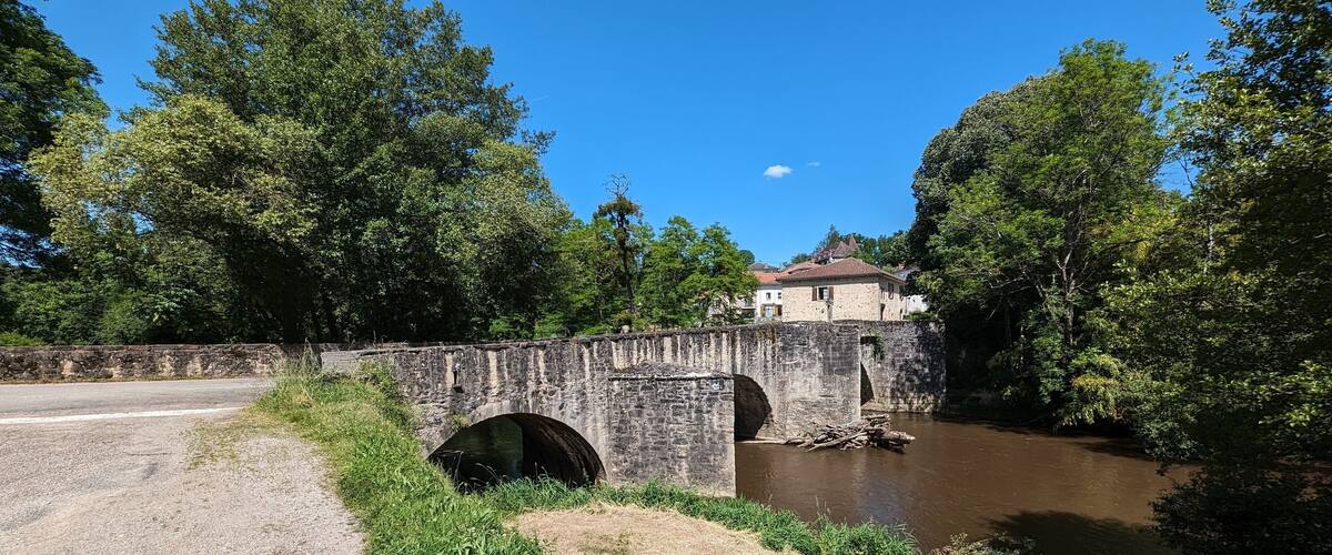 A stone bridge over a river with a house in the background.