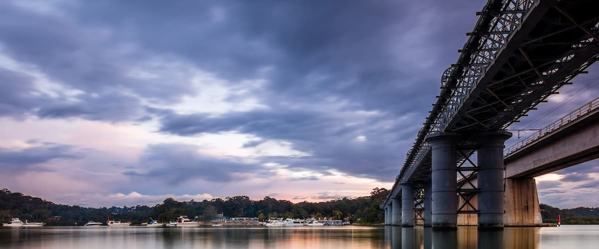 Un grand pont enjambant une étendue d’eau calme, avec des rochers au premier plan et un ciel nuageux.
