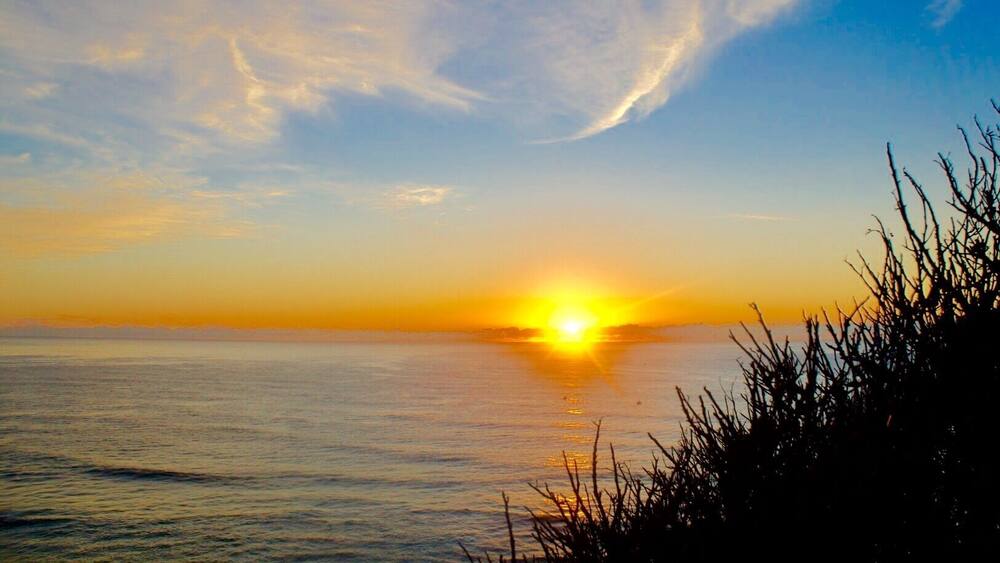 A sunset over a calm sea with a clear sky and distant land.
