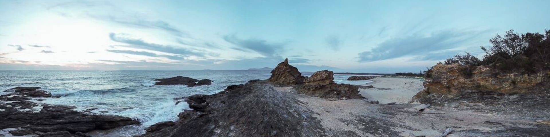 A rocky coastline with waves crashing against the shore and a clear sky.