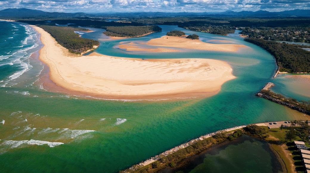 Paesaggio costiero con un'ampia spiaggia sabbiosa, acque cristalline turchesi e montagne sullo sfondo.