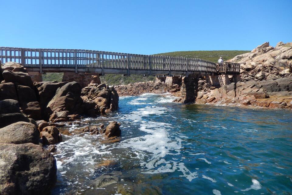 Un puente de madera sobre un río pedregoso con agua azul cristalina.