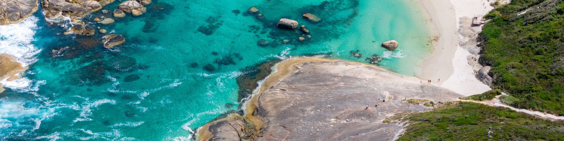 A coastal landscape with turquoise waters, white sandy beaches, and rocky outcrops.
