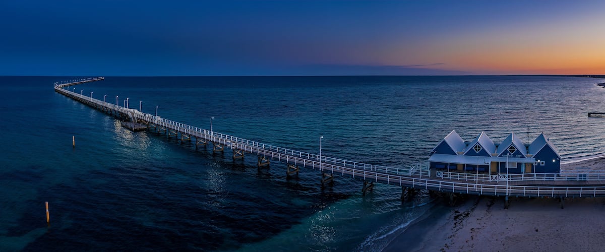 A pier extending into the ocean with a beach and a blue building at the end.
