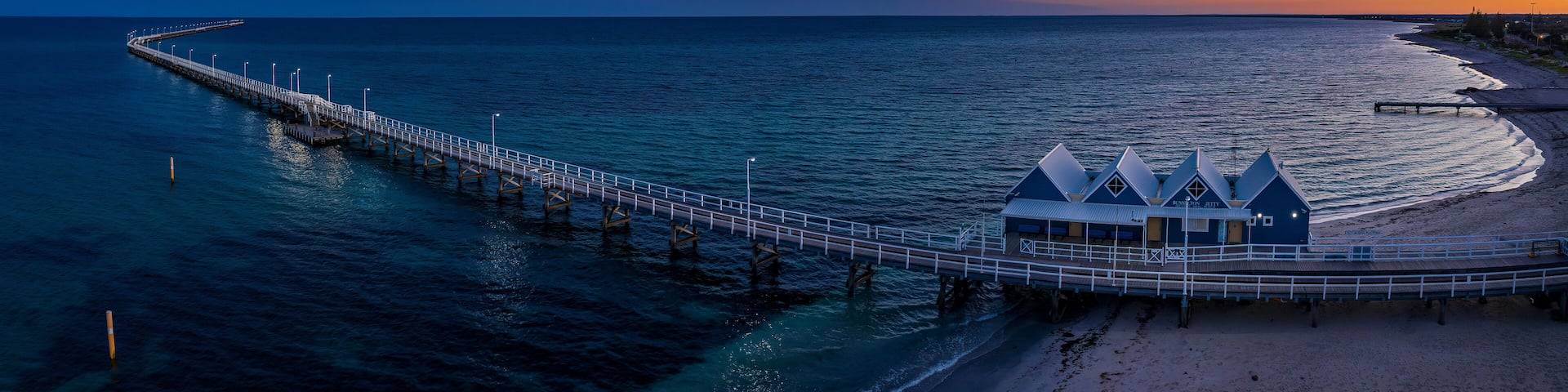 A pier extending into the ocean with a beach and a blue building at the end.