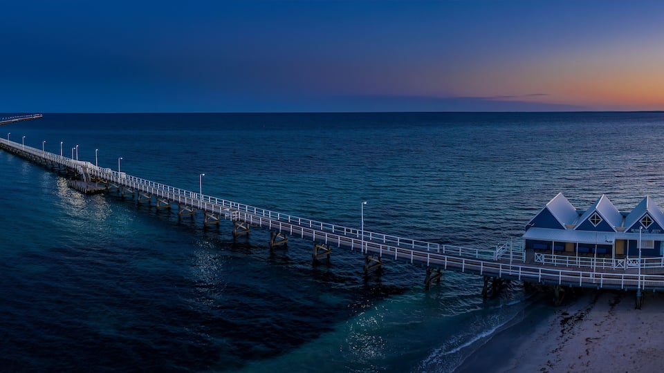 A pier extending into the ocean with a beach and a blue building at the end.