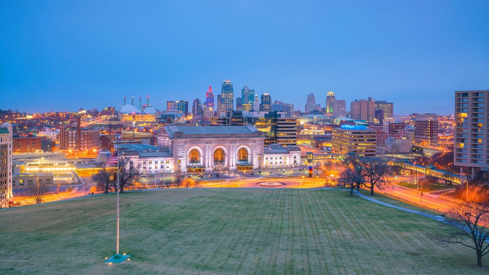 A cityscape at dusk with a prominent historic building in the foreground, surrounded by modern high-rises and illuminated streets.