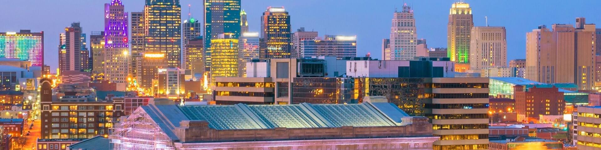 A cityscape with illuminated skyscrapers and a historic building with arched windows.