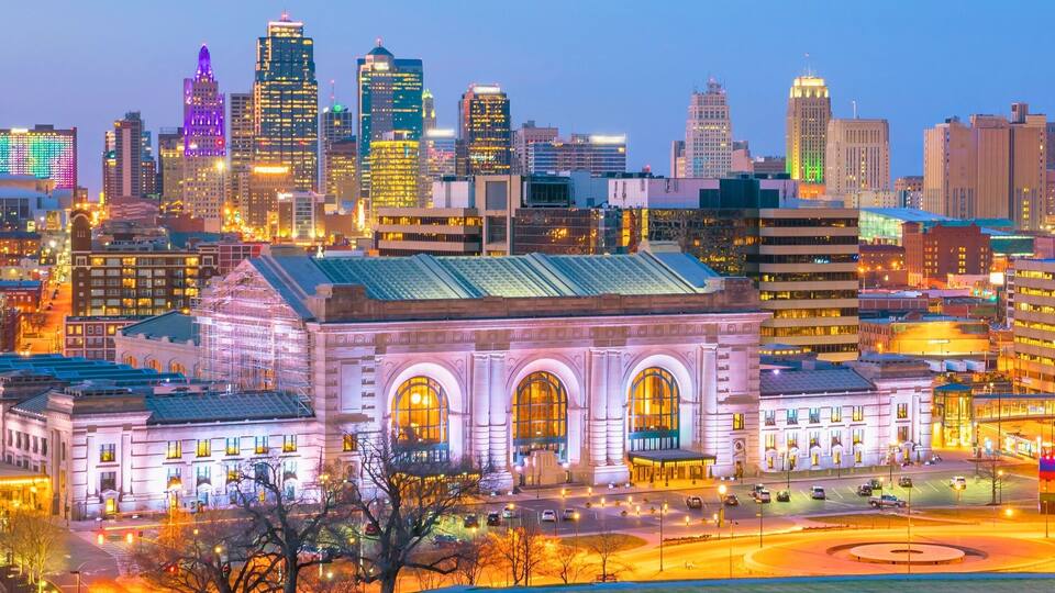 A cityscape with illuminated skyscrapers and a historic building with arched windows.