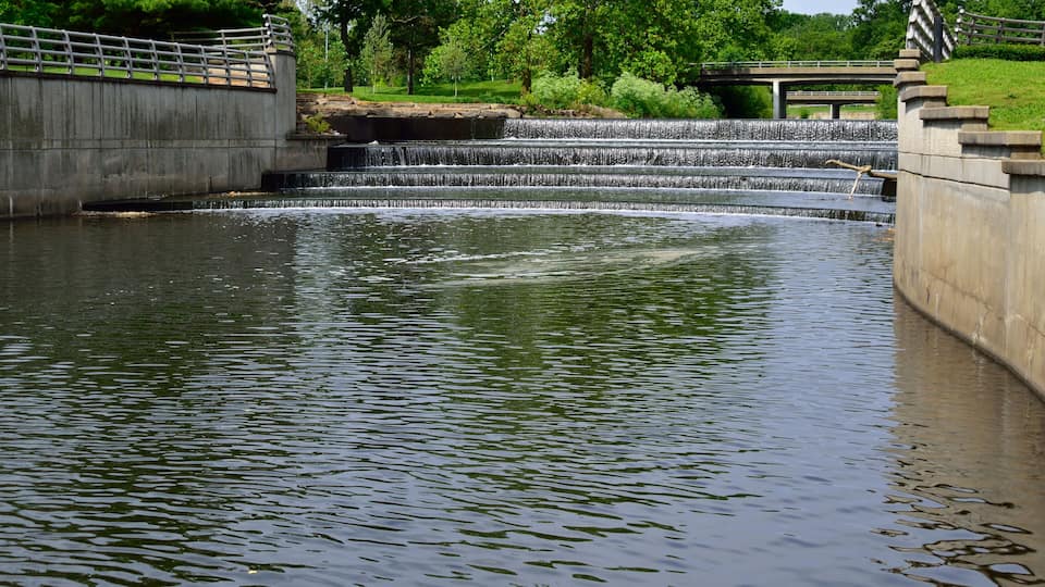 A calm water body with a small waterfall and a stone bridge.