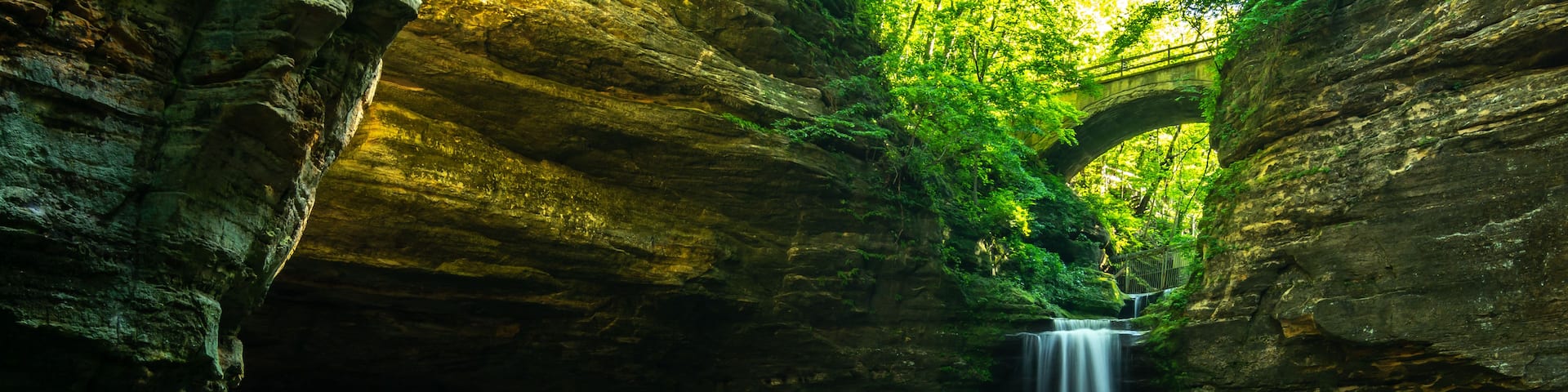 A serene waterfall in a rocky gorge with moss-covered walls and a clear stream.