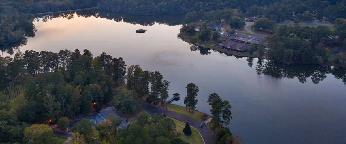 A lake surrounded by dense forest, a small island, and a distant town with buildings and roads.