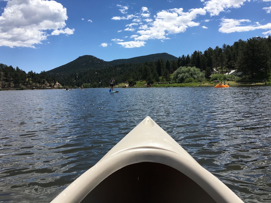 Un kayak sur un lac paisible, avec des montagnes en arrière-plan et un ciel partiellement nuageux.