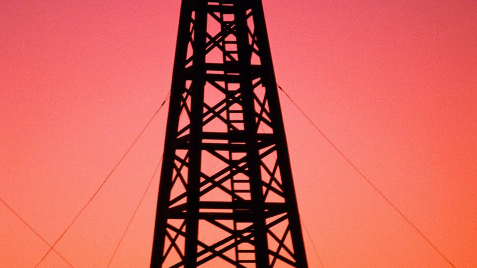 A silhouette of a tall transmission tower against a sunset sky.