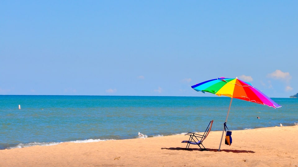 A beach with a colorful umbrella, a chair, and the ocean.
