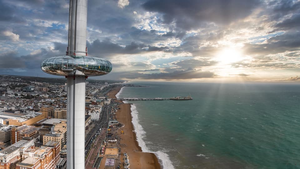A coastal cityscape with a prominent tower, a beach, and a pier extending into the sea.