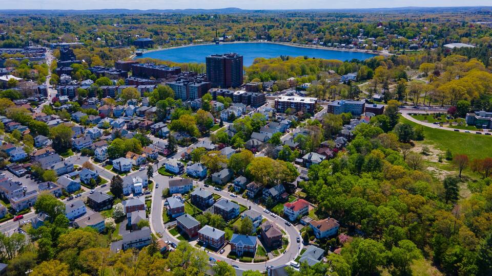 An aerial view of a residential area with houses, a large lake, and surrounding greenery.