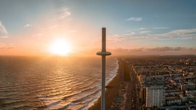 Magical sunset aerial view of British Airways i360 viewing tower pod with tourists in Brighton, UK with sea and Brighton Palace Pier in the background.