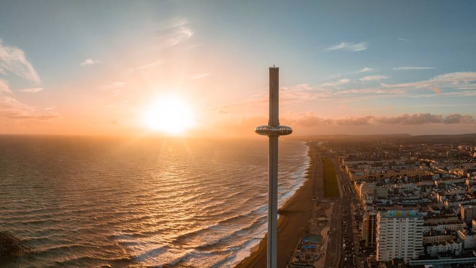 A coastal cityscape with a prominent tower, a beach, and the ocean during sunset.