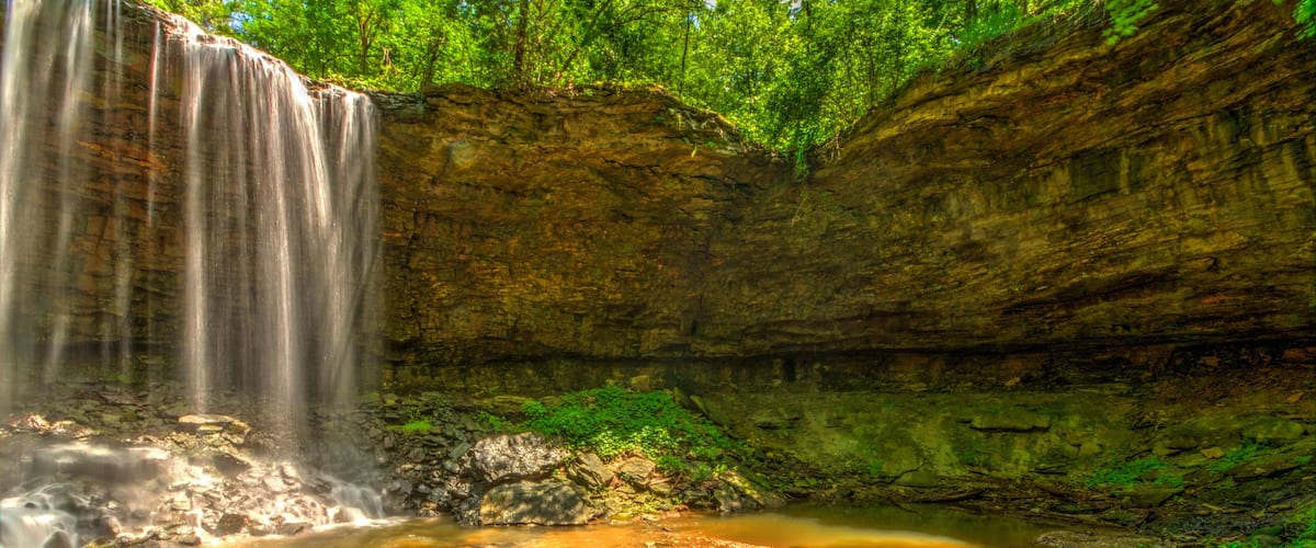 A waterfall cascading into a pool surrounded by rocky terrain and lush greenery.