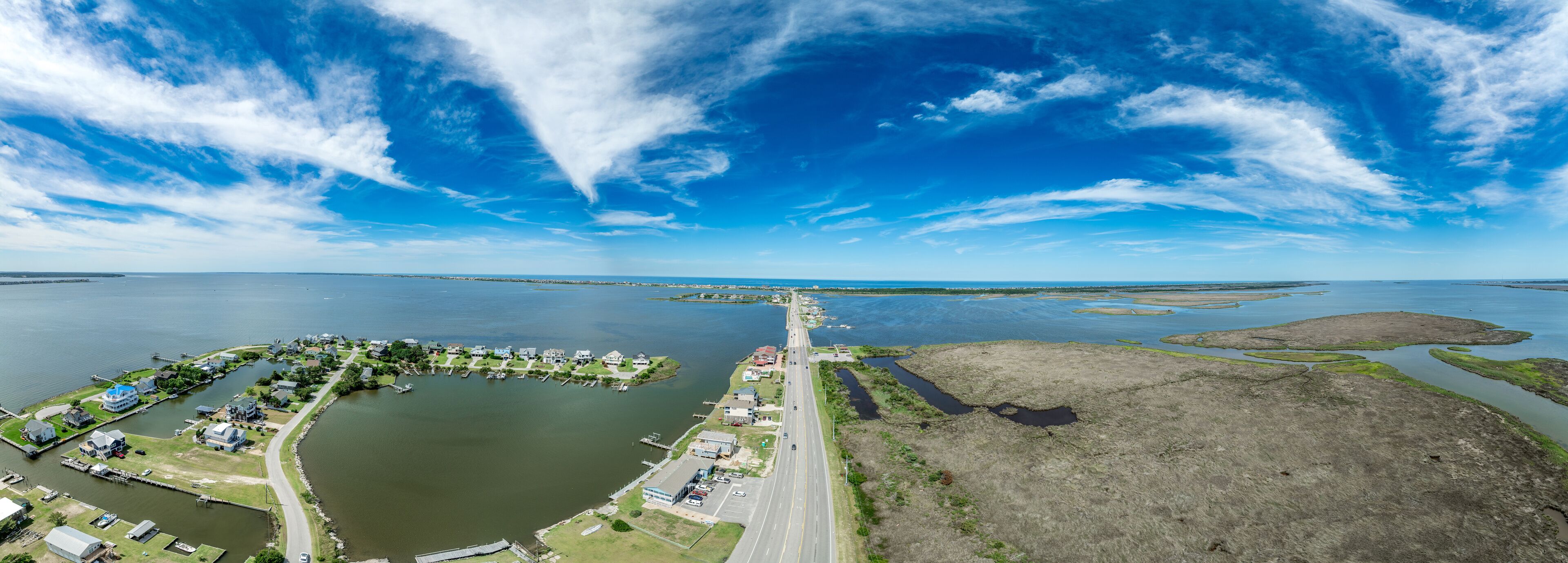 An aerial view of a coastal town with a marina, houses, and a bridge connecting to the mainland.