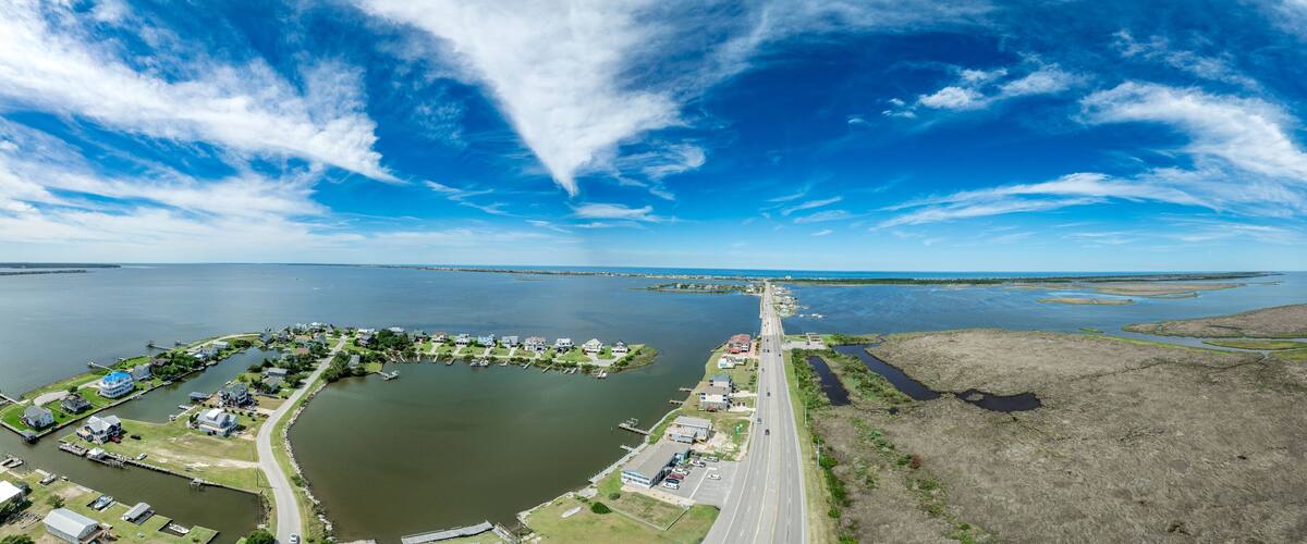 An aerial view of a coastal town with a marina, houses, and a bridge connecting to the mainland.
