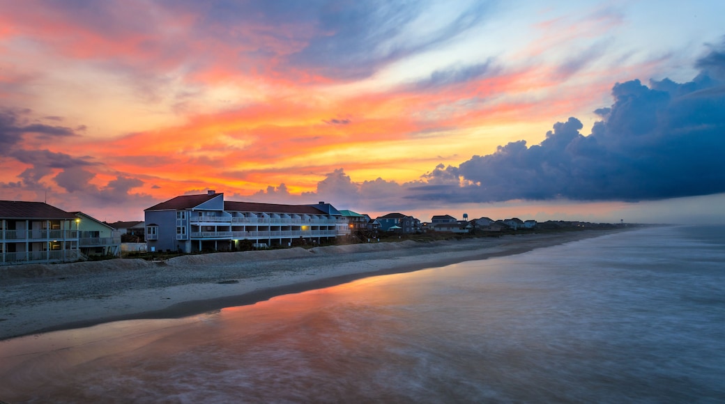 Une plage bordée d’une rangée de maisons, avec un coucher de soleil en toile de fond.
