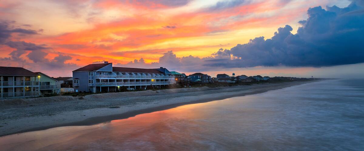 A beach with a row of houses and a sunset.