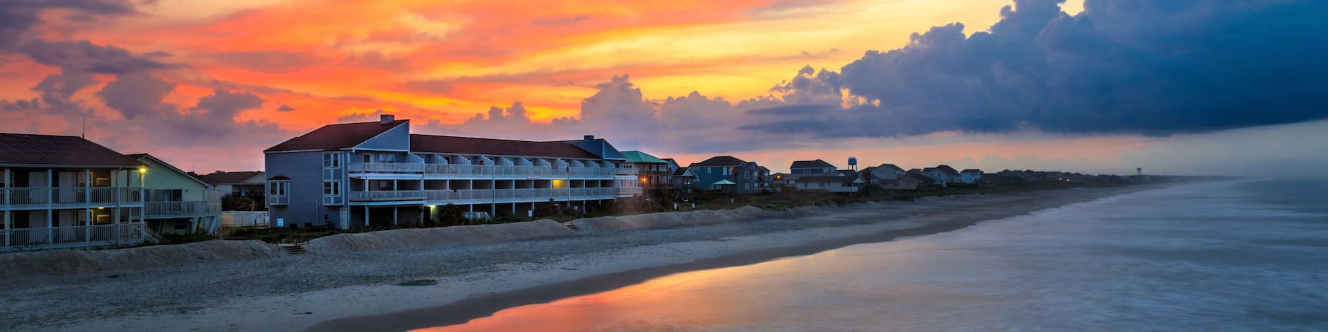 A beach with a row of houses and a sunset.