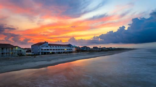 Une plage bordée d’une rangée de maisons, avec un coucher de soleil en toile de fond.
