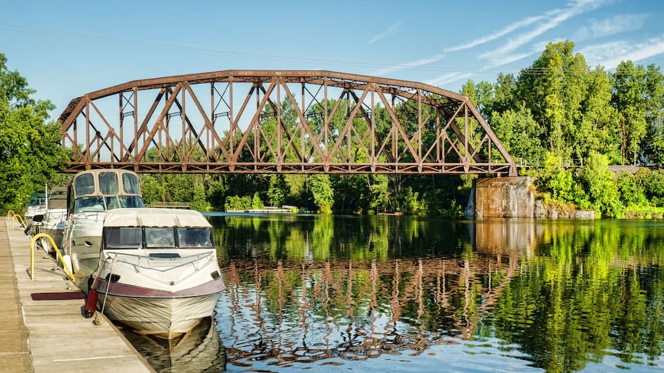 A white boat docked at a pier with a large metal bridge in the background.