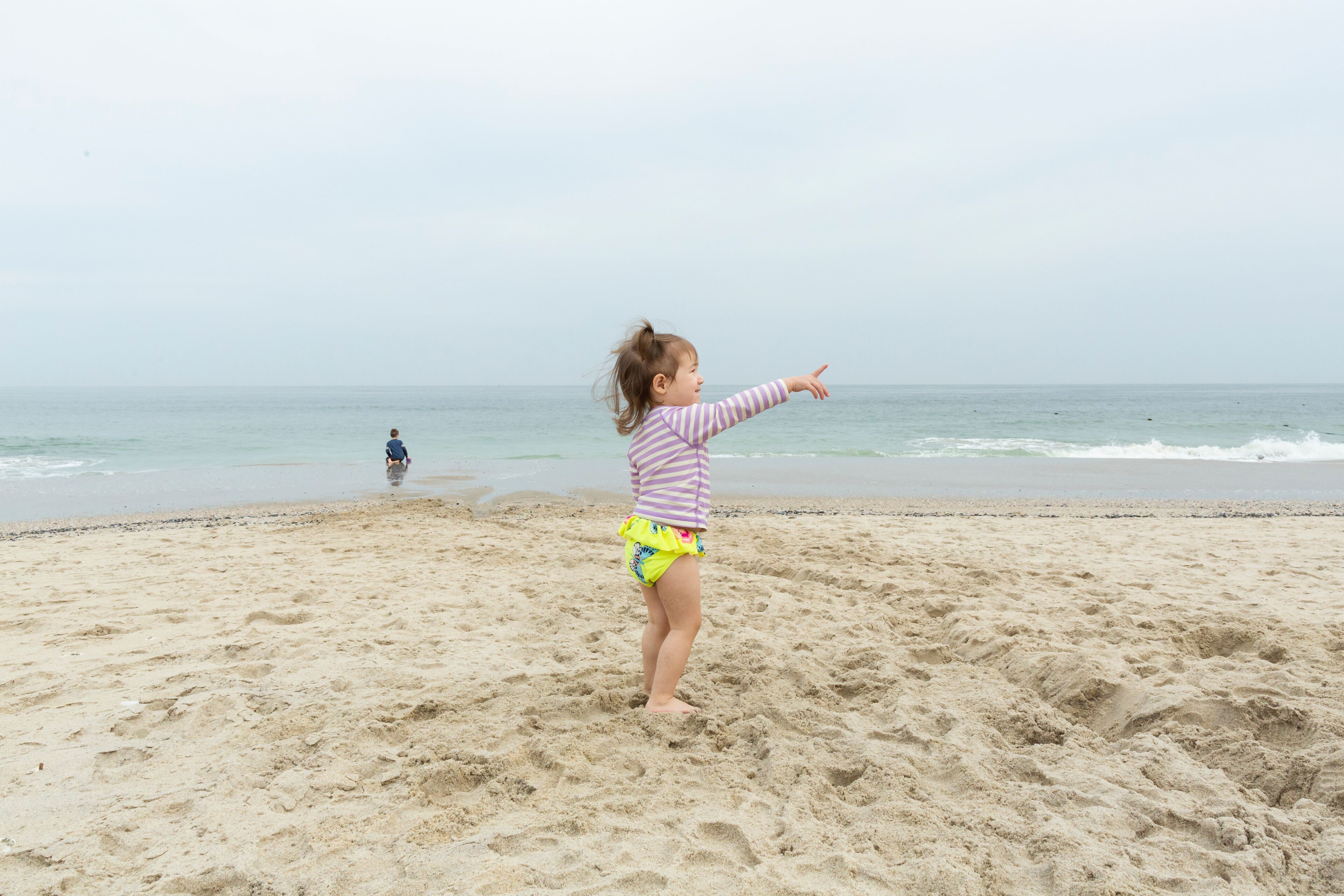 Una playa arenosa con un niño señalando hacia el océano.