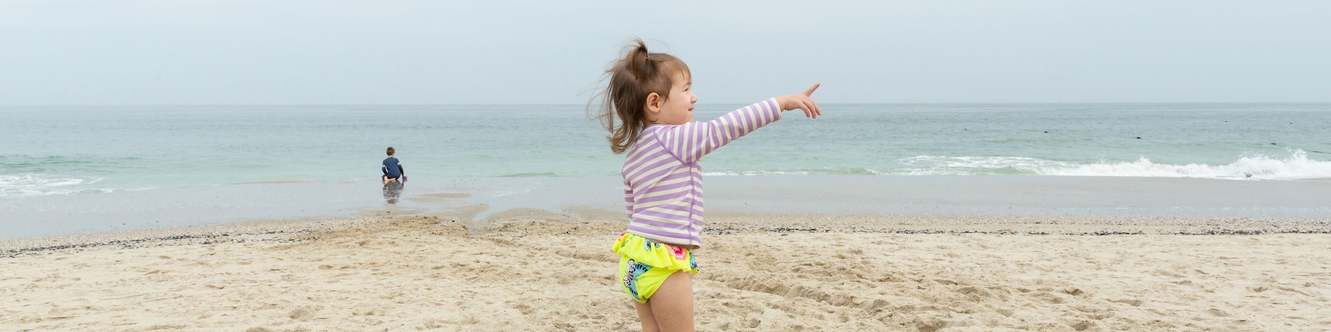 Una playa arenosa con un niño señalando hacia el océano.