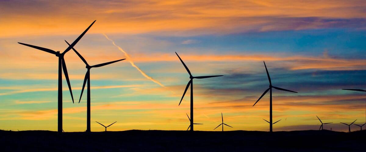 A landscape with multiple wind turbines silhouetted against a colorful sunset sky.
