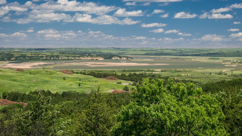 A green valley with a river, a bridge, and a forested area.