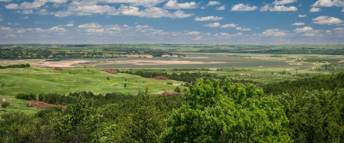 A green valley with a river, a bridge, and a forested area.
