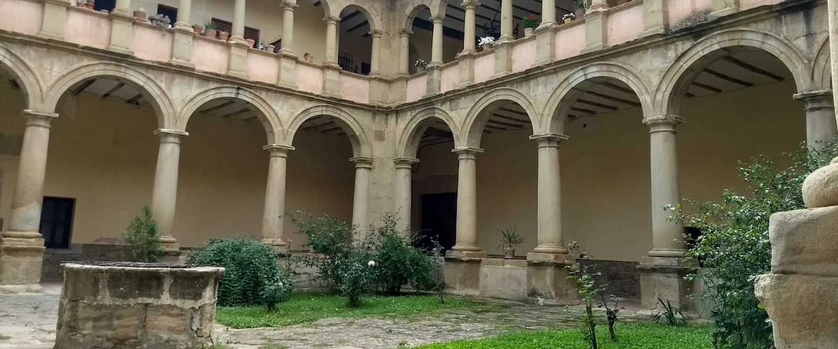 A courtyard with arches and columns, surrounded by greenery and potted plants.