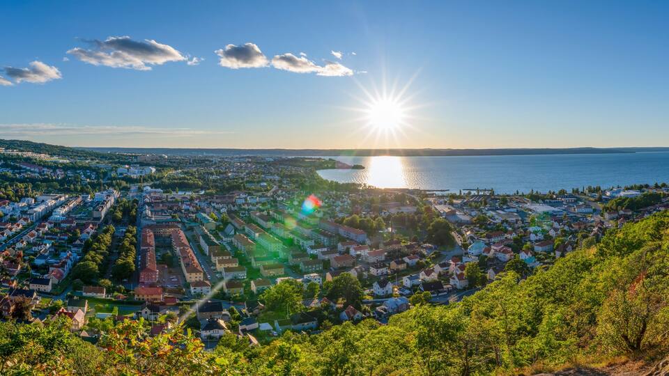 A coastal cityscape with a sunlit sea, dense residential area, and surrounding hills.