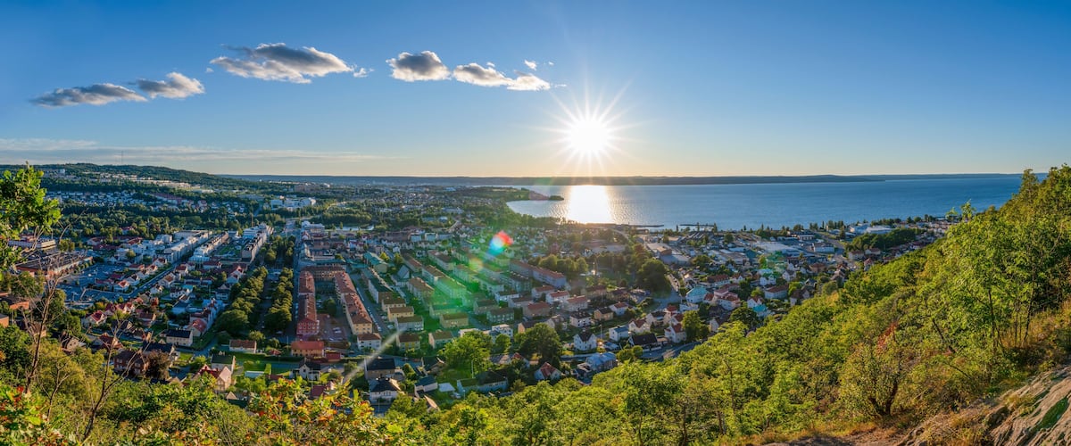 A coastal cityscape with a sunlit sea, dense residential area, and surrounding hills.