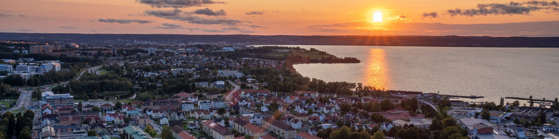 Paisagem costeira ao pôr do sol com edifícios residenciais, um corpo d'água e uma ponte ao longe.