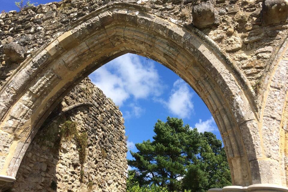 Un antiguo arco de piedra con un cielo azul claro y un árbol al fondo.