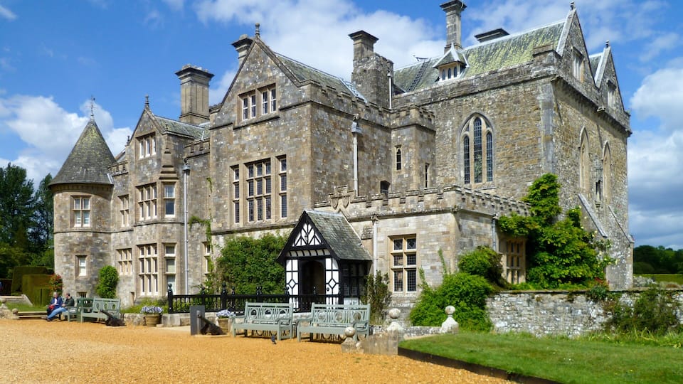 A large stone building with multiple towers and a small Tudor-style structure in front.
