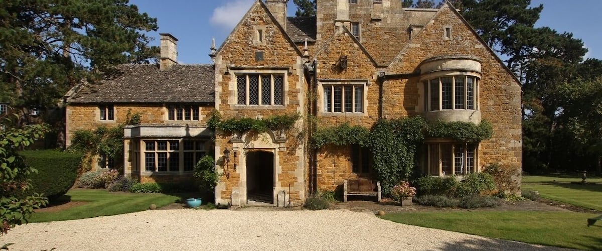 A large stone house with a traditional design, surrounded by a well-maintained garden and trees.