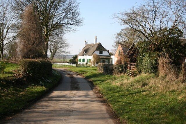 A narrow rural road leading to a white house with a thatched roof.
