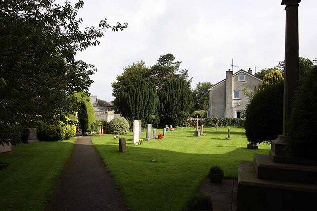 A cemetery with a pathway, headstones, and a house in the background.