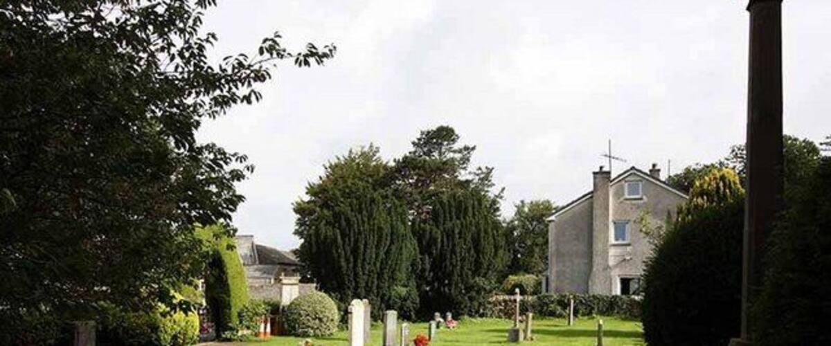 A cemetery with a pathway, headstones, and a house in the background.