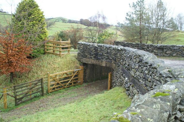 A stone bridge over a small stream, surrounded by grassy fields and trees.